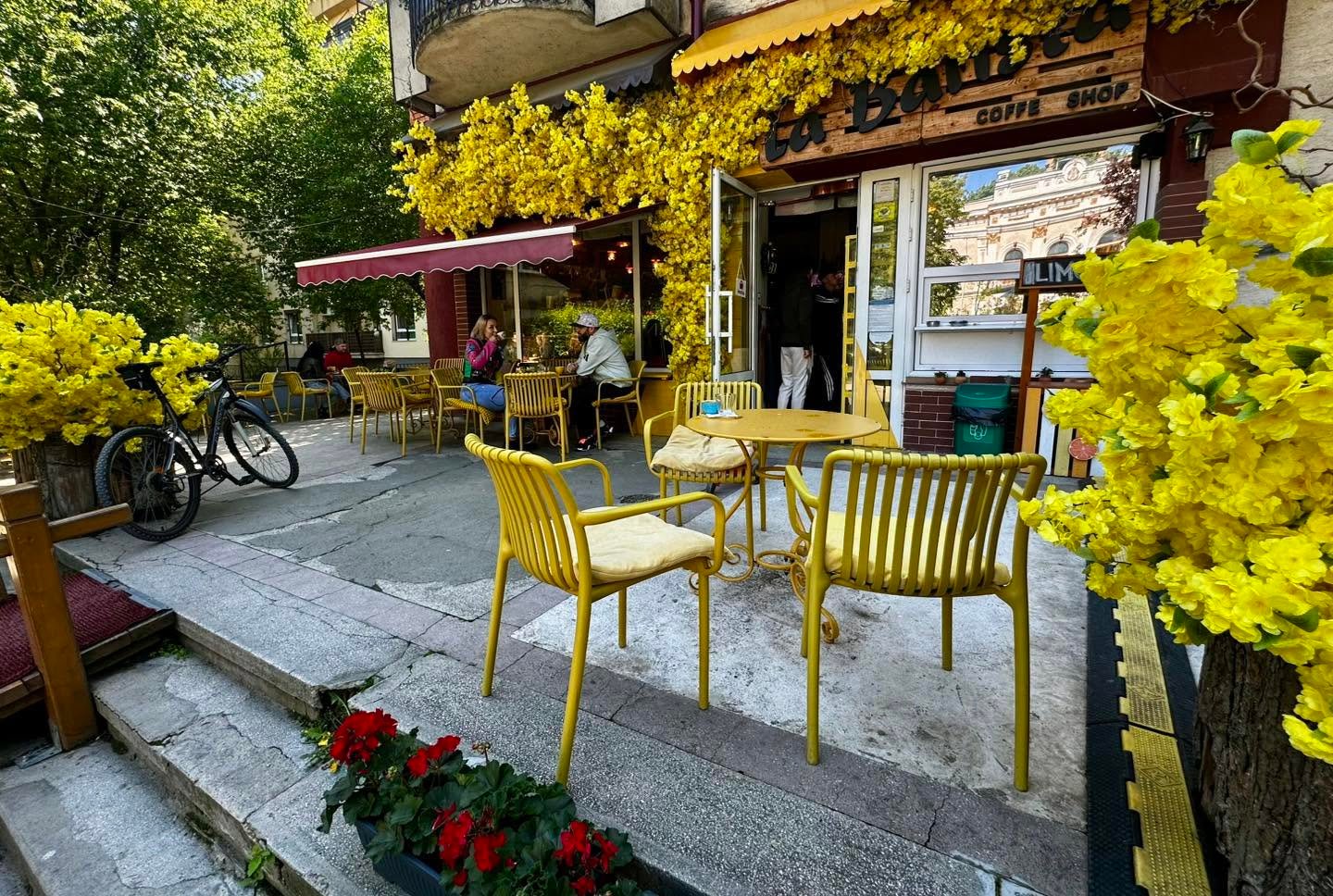 Terasa La Barista, cu scaune galbene și intrarea decorată cu flori