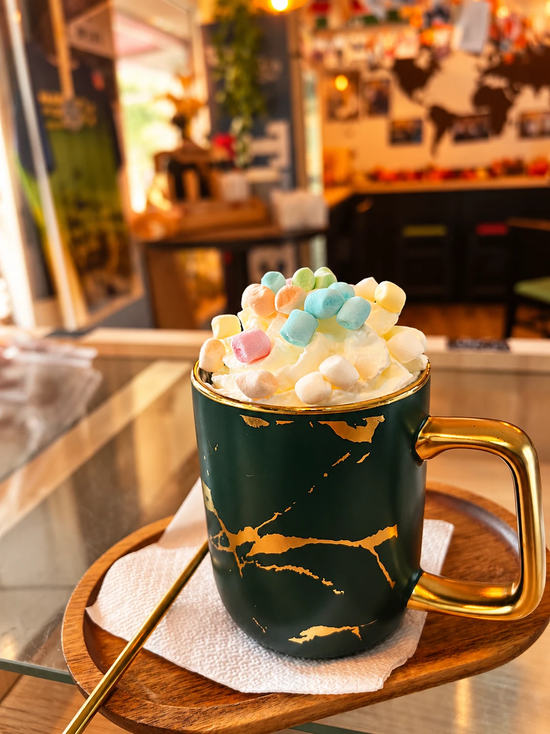 Ciocolată caldă cu frișcă și marshmallows, în cana verde și aurie La Barista