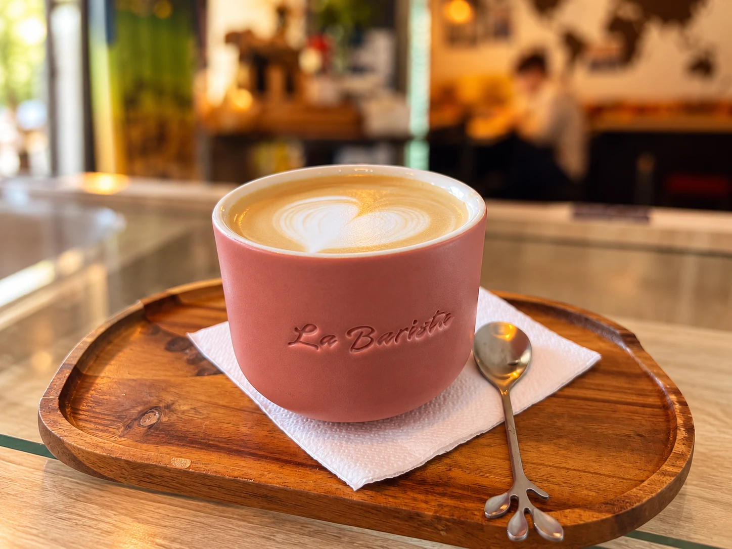 Latte cu latte art în ceașca roz La Barista, pe tava de lemn